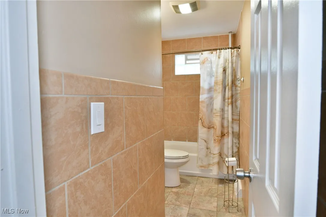 Bathroom featuring tile walls, shower / bath combo with shower curtain, and tile patterned floors