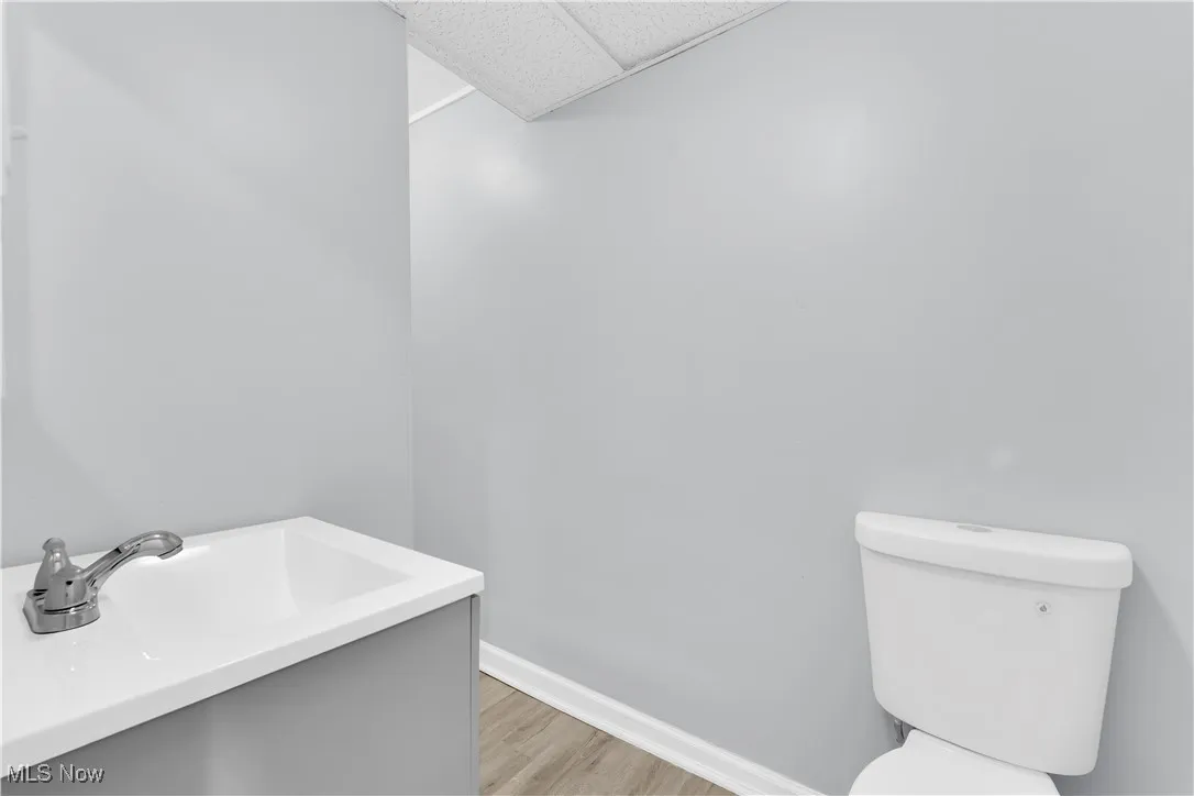 Half bath with vanity, a paneled ceiling, and light wood-style flooring
