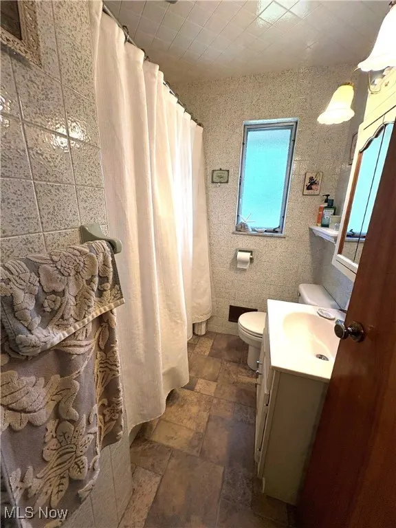 Full bathroom featuring vanity, tile walls, curtained shower, and toilet