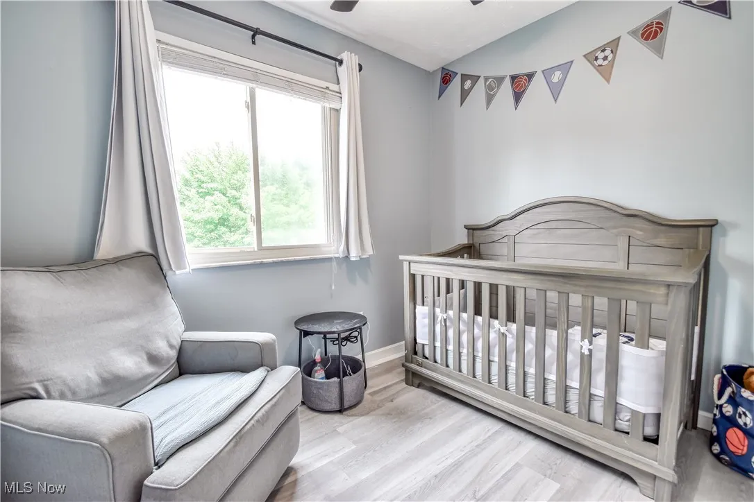 Bedroom with light wood-style floors, a nursery area, and ceiling fan