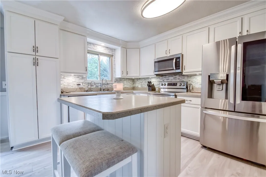 Kitchen featuring stainless steel appliances, a kitchen island, white cabinets, and a breakfast bar area
