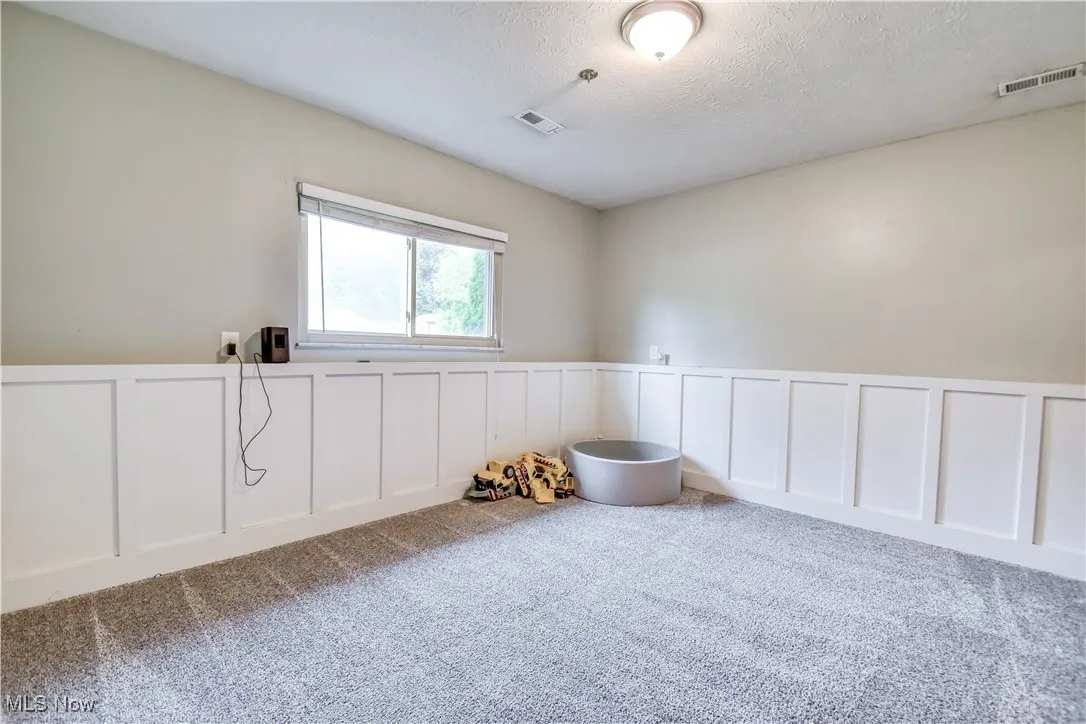 Spare room featuring a decorative wall, a wainscoted wall, carpet floors, and a textured ceiling