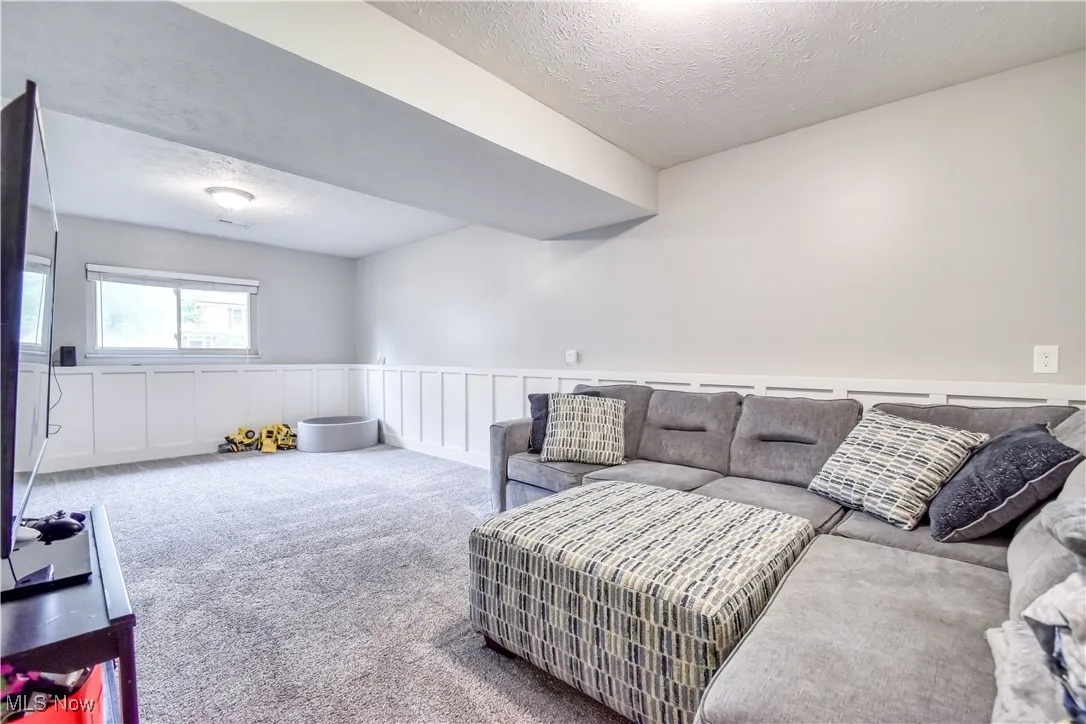 Living room with carpet floors, a textured ceiling, a wainscoted wall, and a decorative wall