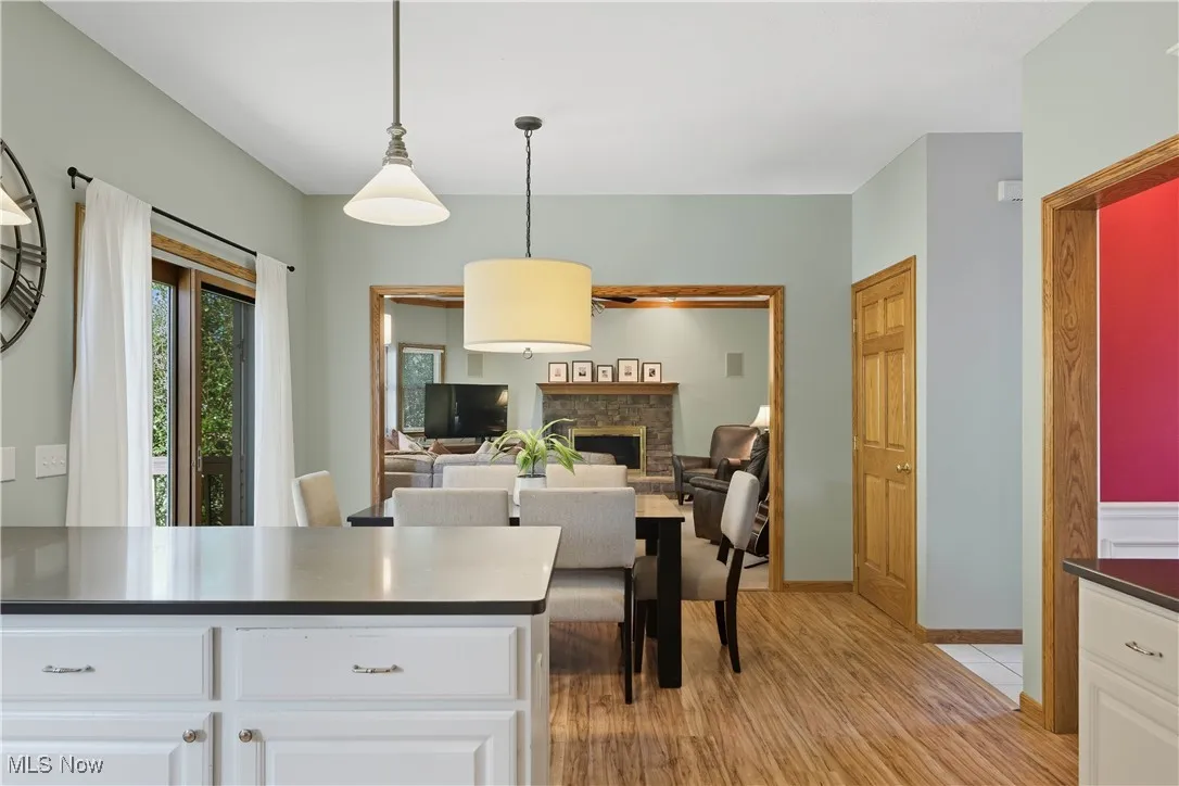 Kitchen featuring a stone fireplace, light wood finished floors, hanging light fixtures, white cabinetry, and open floor plan