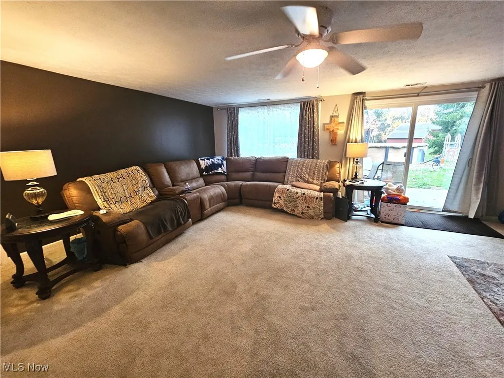 Carpeted living room with a textured ceiling and ceiling fan