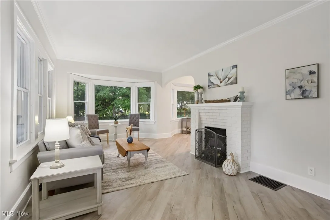 Living room with crown molding, a fireplace, light wood finished floors, and arched walkways