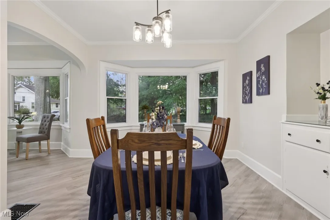 Dining space with crown molding, light wood-style floors, arched walkways, and a chandelier