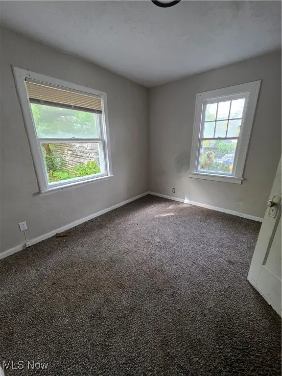 Unfurnished room with dark colored carpet and healthy amount of natural light