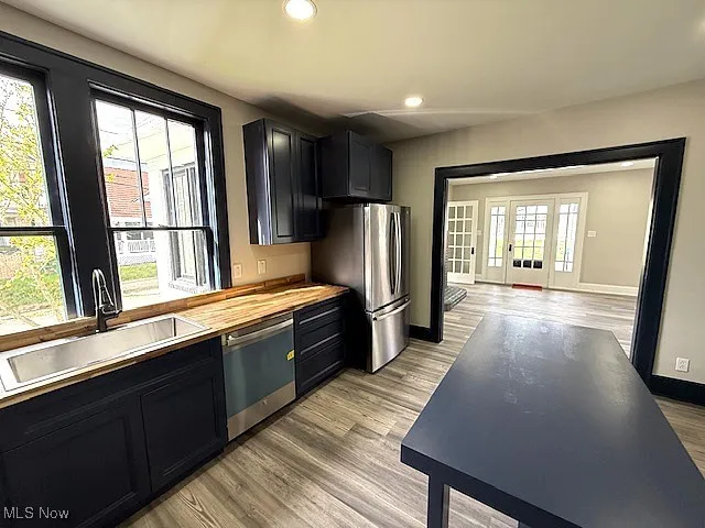 Kitchen with recessed lighting, light wood-style flooring, dark cabinetry, appliances with stainless steel finishes, and butcher block counters