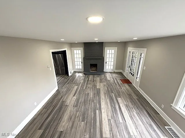 Unfurnished living room featuring dark wood-type flooring, a brick fireplace, and recessed lighting