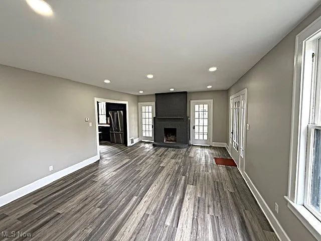 Unfurnished living room with recessed lighting, dark wood-style flooring, and a brick fireplace