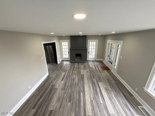 Unfurnished living room with dark wood-style floors, recessed lighting, and a brick fireplace