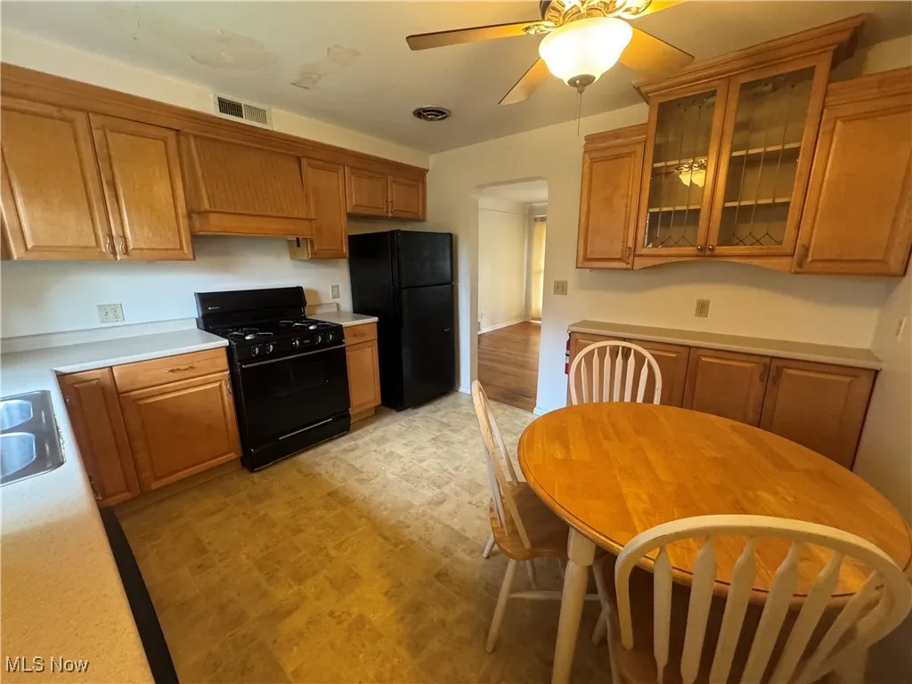 Kitchen featuring brown cabinets, black appliances, light countertops, and a ceiling fan