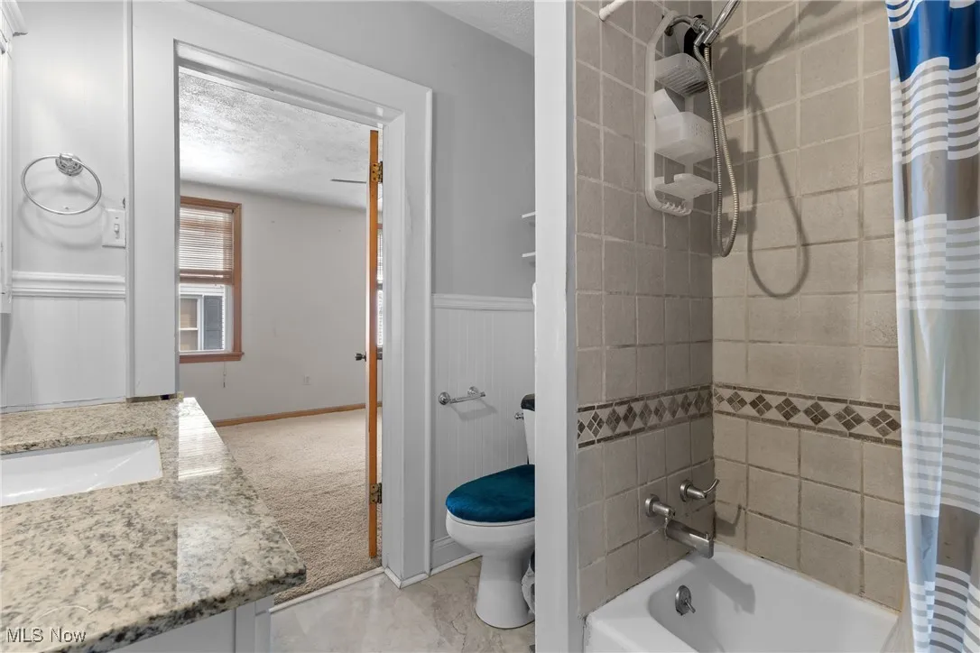 Full bath with shower / tub combo, vanity, a textured ceiling, and light tile patterned floors