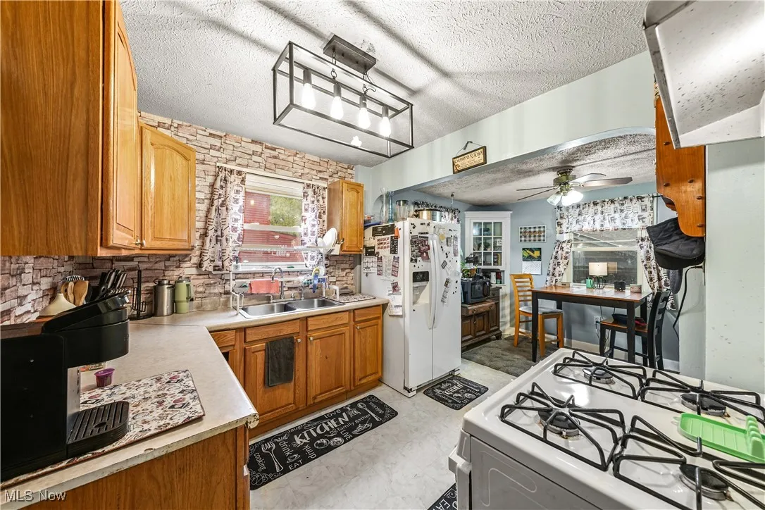 Kitchen featuring white appliances, a textured ceiling, range hood, light countertops, and brown cabinetry
