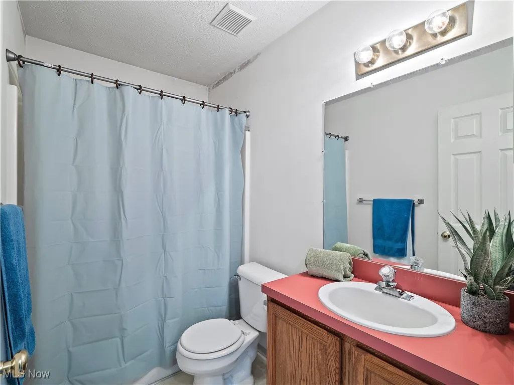 Full bathroom with a textured ceiling, vanity, and shower / tub combo with curtain