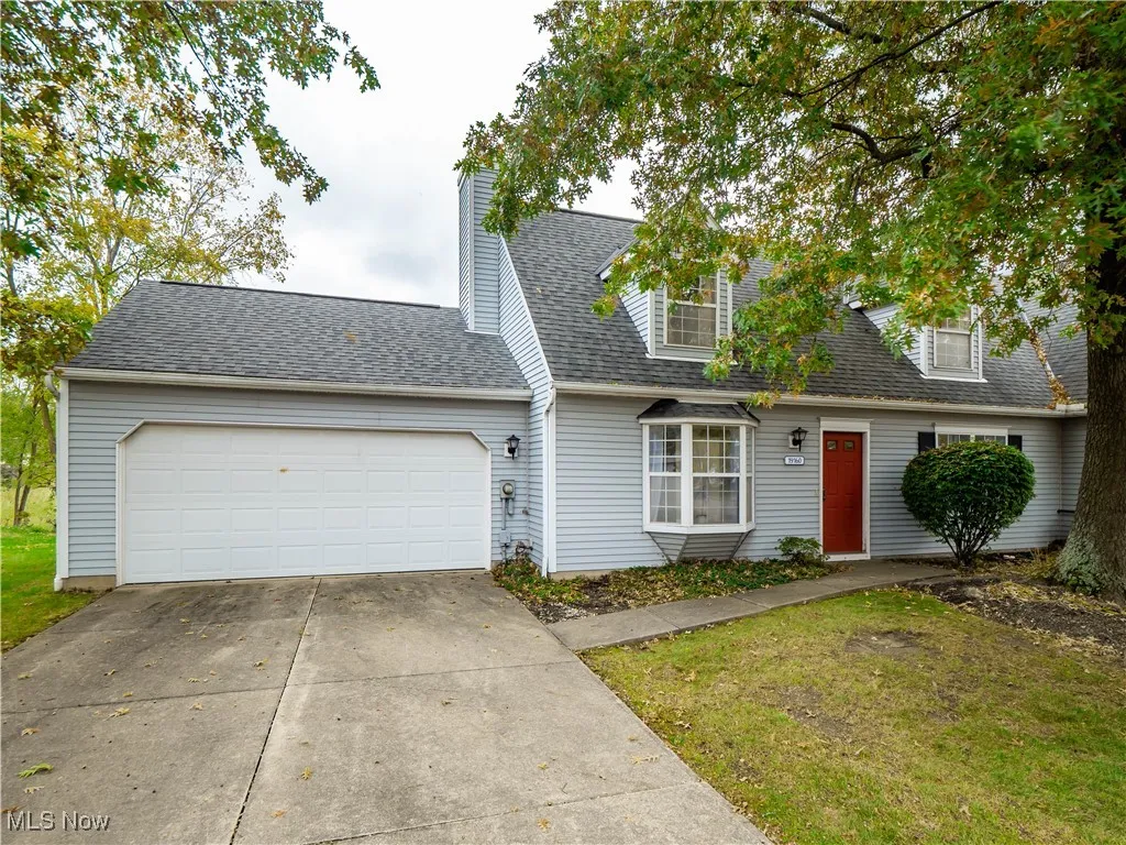 Cape cod home with a shingled roof, driveway, a garage, a front yard, and a chimney