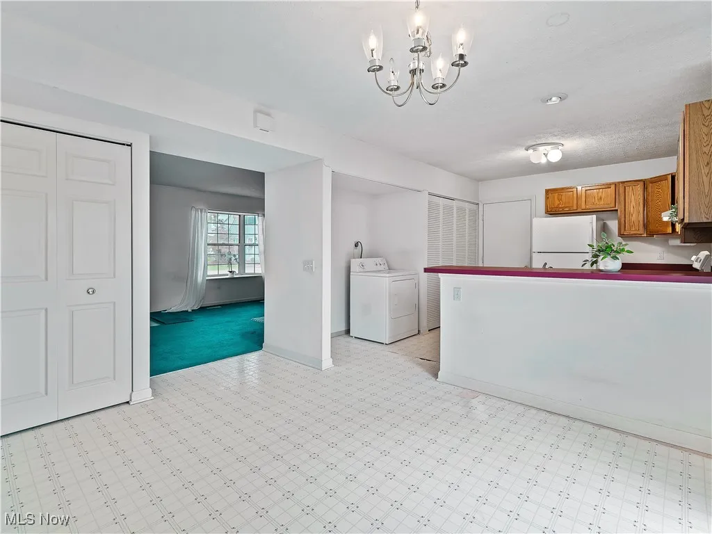Kitchen with washer / dryer, a chandelier, brown cabinetry, dark countertops, and freestanding refrigerator