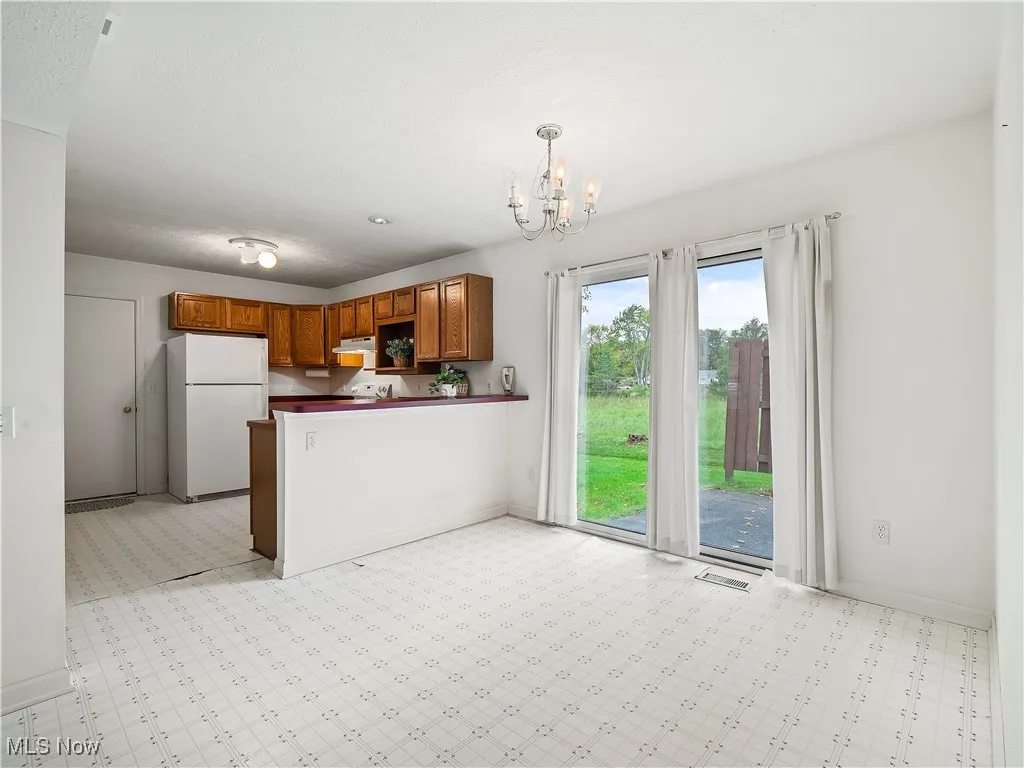 Kitchen with brown cabinets, dark countertops, freestanding refrigerator, a peninsula, and hanging light fixtures