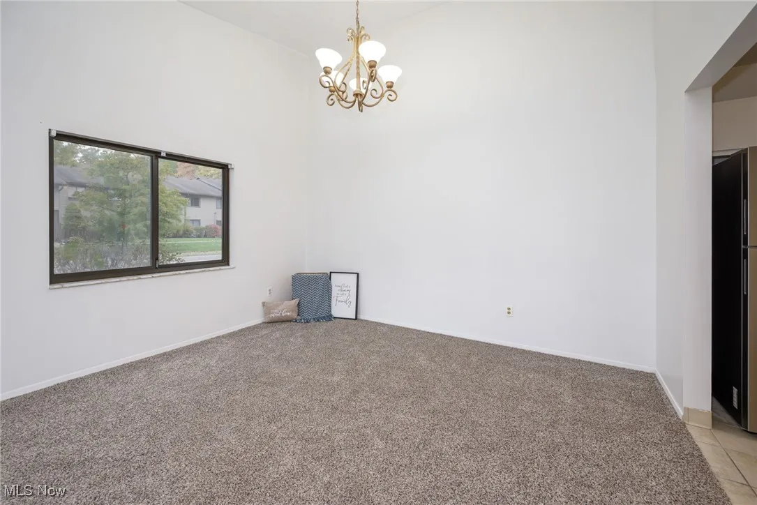 Unfurnished room featuring a high ceiling, light colored carpet, and a chandelier