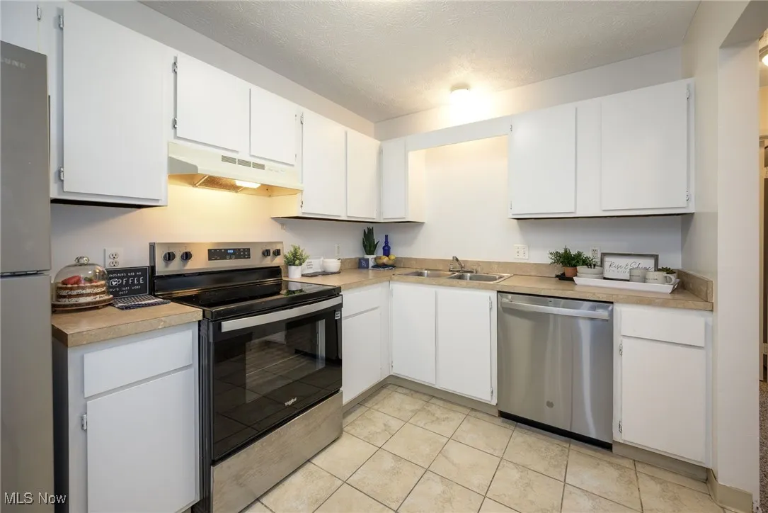Kitchen featuring appliances with stainless steel finishes, white cabinetry, a textured ceiling, under cabinet range hood, and light countertops