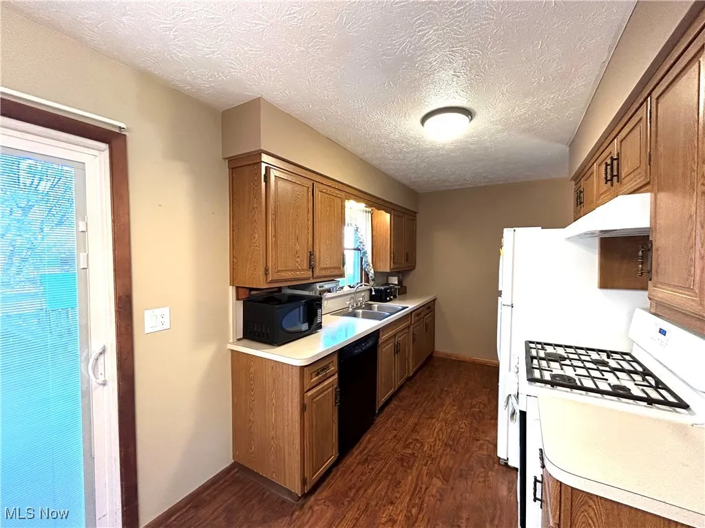 Kitchen with black appliances, dark wood finished floors, a textured ceiling, light countertops, and brown cabinets