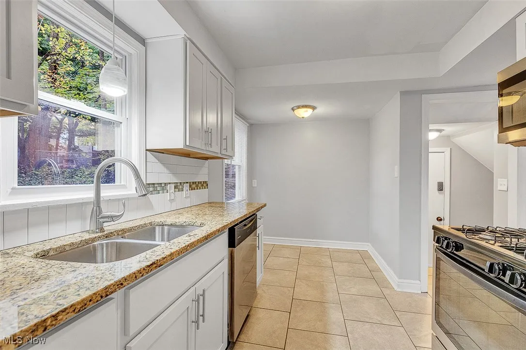Kitchen featuring light stone counters, light tile patterned floors, stainless steel appliances, white cabinetry, and tasteful backsplash