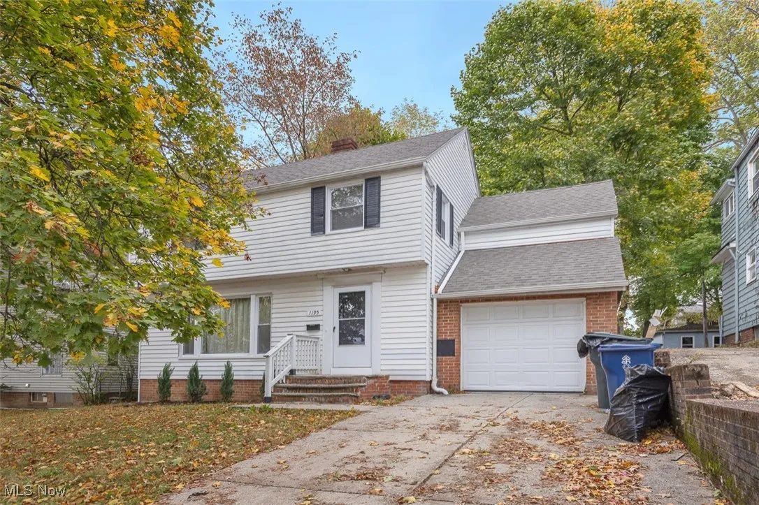 Colonial-style house featuring a shingled roof, concrete driveway, an attached garage, and brick siding
