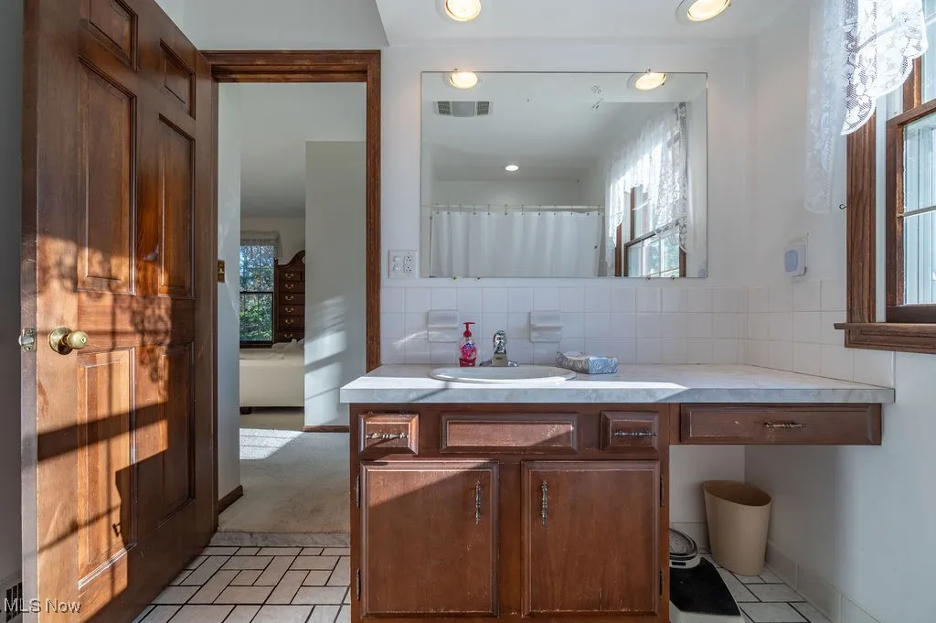 Bathroom with light tile patterned floors, backsplash, vanity, and healthy amount of natural light