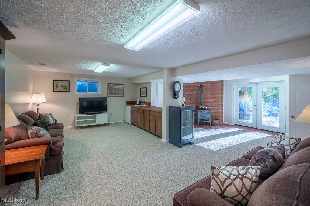 Living area with a wood stove, light colored carpet, a textured ceiling, and french doors