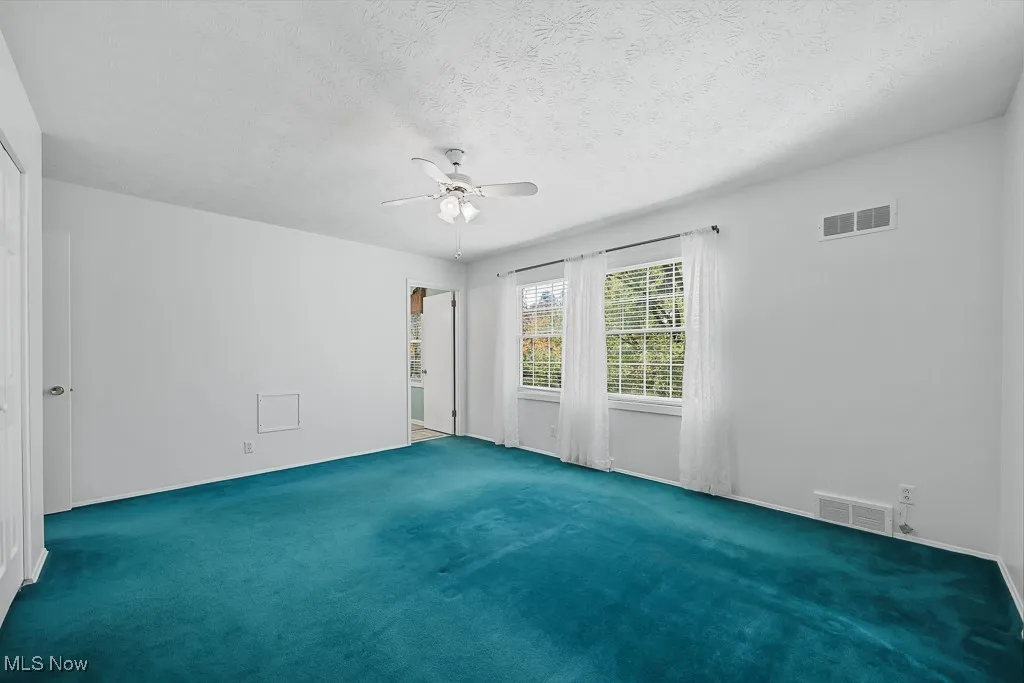 Empty room with carpet floors, ceiling fan, and a textured ceiling