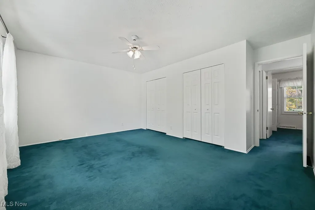 Unfurnished bedroom with two closets, dark carpet, and ceiling fan