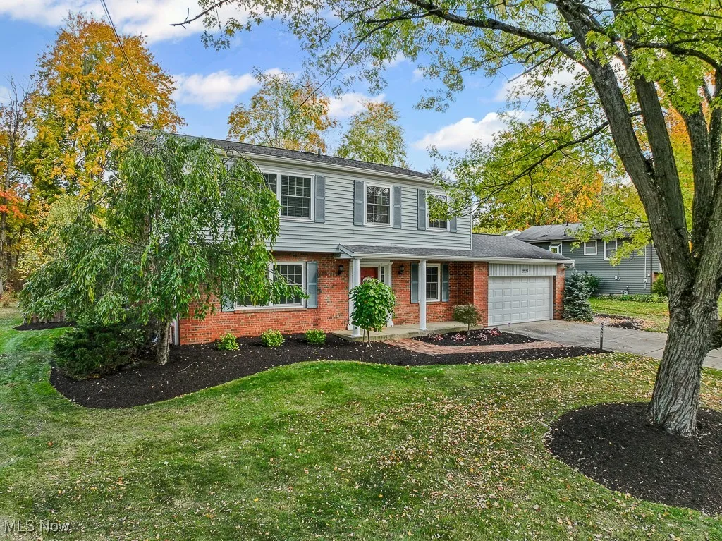 View of front facade featuring brick siding, driveway, a front lawn, an attached garage, and a porch