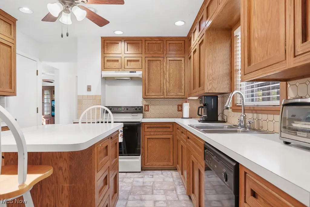 Kitchen with a breakfast bar, backsplash, brown cabinets, dishwasher, and recessed lighting