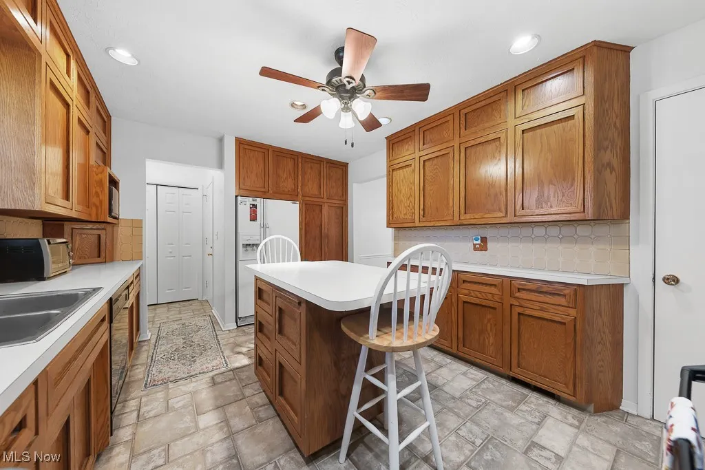 Kitchen featuring decorative backsplash, light countertops, brown cabinetry, a kitchen island, and recessed lighting