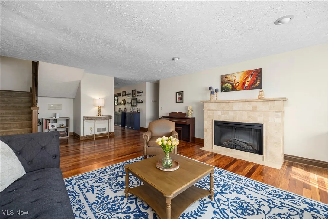 Living room with a tiled fireplace, dark wood-style flooring, stairway, and a textured ceiling