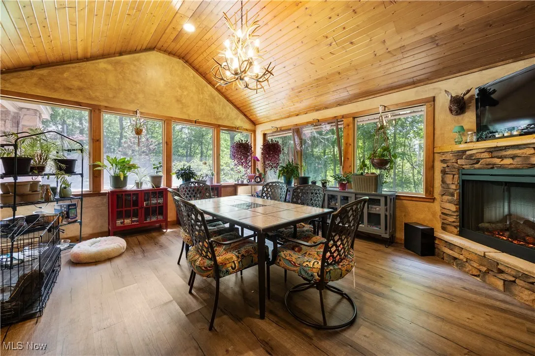 Dining room with wood-type flooring, wooden ceiling, a stone fireplace, a chandelier, and high vaulted ceiling