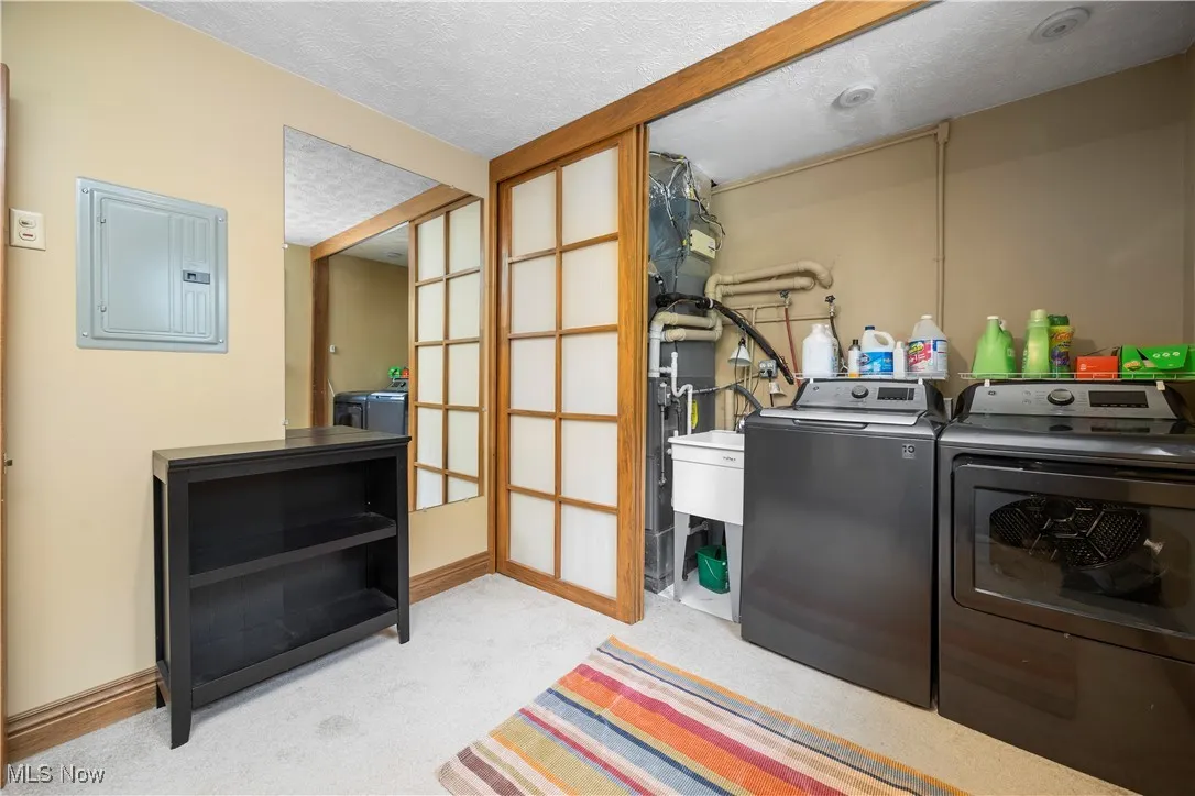 Laundry room featuring electric panel, separate washer and dryer, a textured ceiling, and light colored carpet