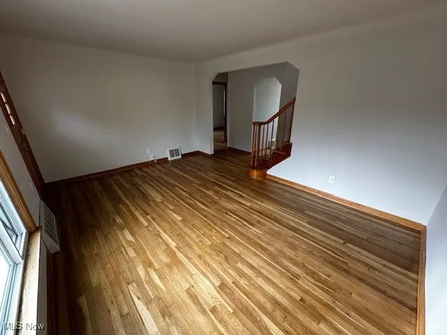 Empty room with wood-type flooring, arched walkways, and stairway