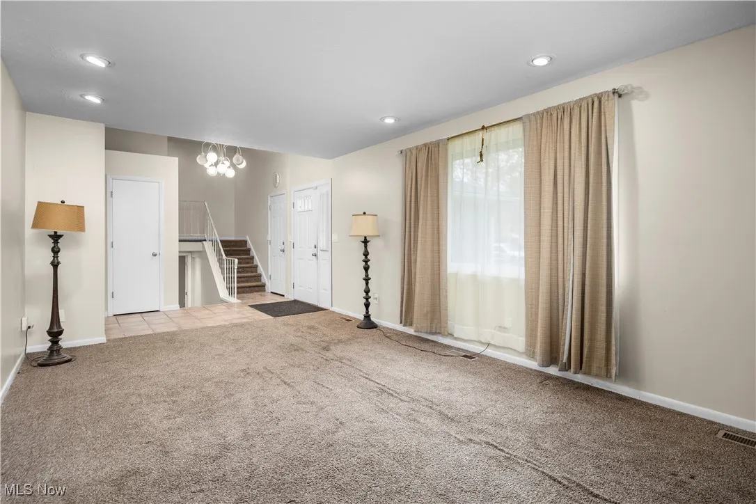 Unfurnished living room featuring carpet floors, a chandelier, recessed lighting, and stairs