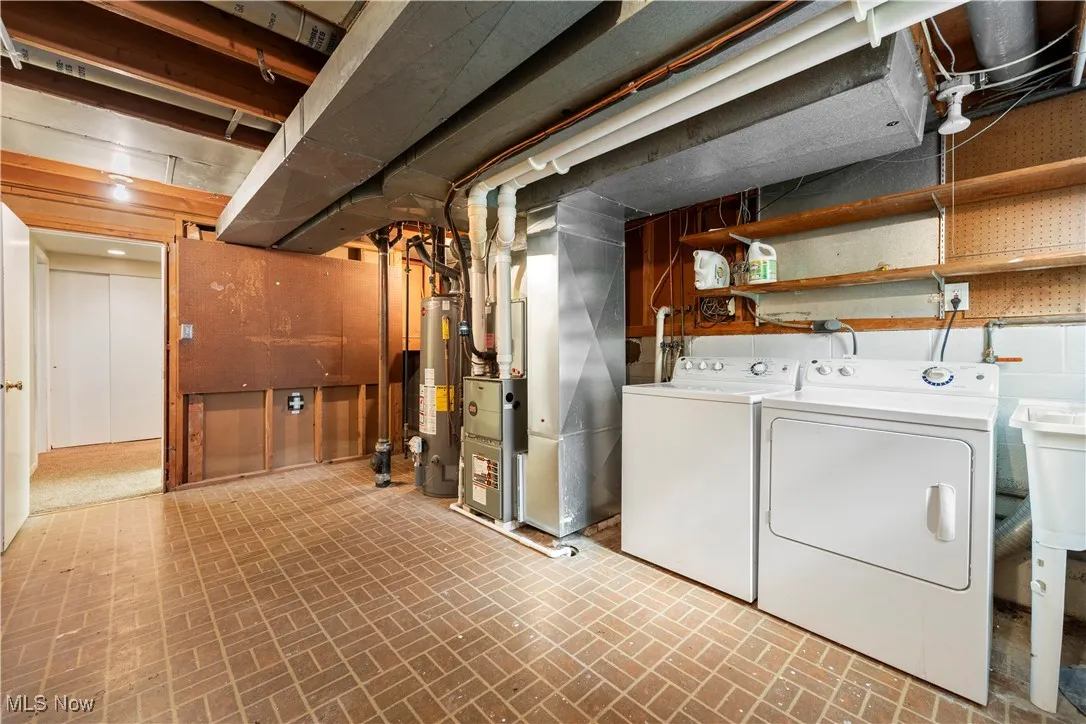 Unfinished below grade area with brick patterned floors, water heater, heating unit, and washing machine and clothes dryer