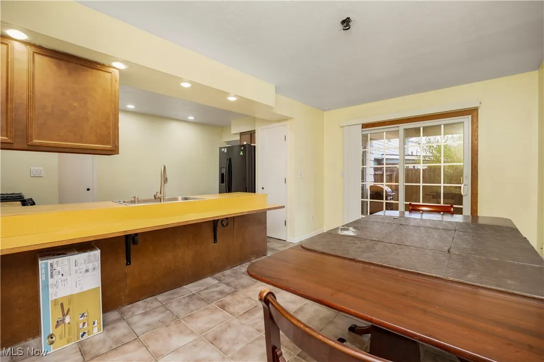 Kitchen with brown cabinets, light countertops, a peninsula, recessed lighting, and black refrigerator with ice dispenser