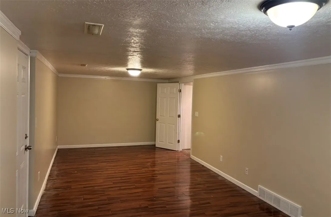 Unfurnished room featuring a textured ceiling, dark wood-style floors, and crown molding