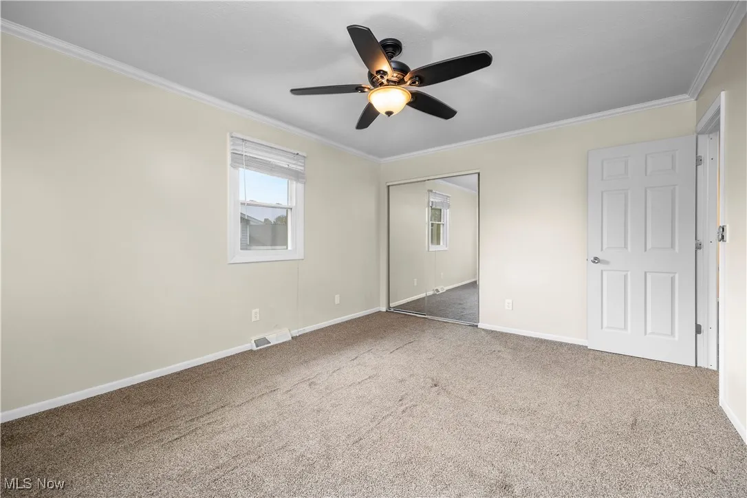 Unfurnished bedroom with crown molding, carpet flooring, a closet, and ceiling fan