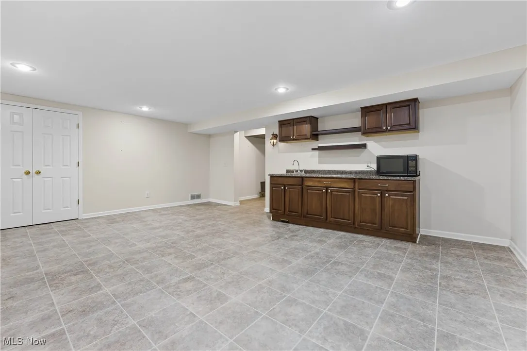 Kitchen featuring dark brown cabinets, recessed lighting, black microwave, light tile patterned floors, and open shelves