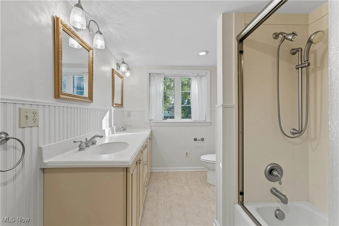 Bathroom featuring a wainscoted wall, double vanity, shower / bath combination, recessed lighting, and light tile patterned floors