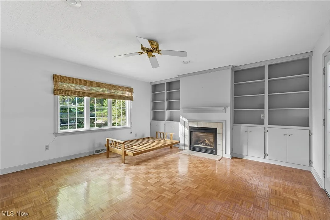 Unfurnished living room featuring built in shelves, a tile fireplace, ceiling fan, and a textured ceiling