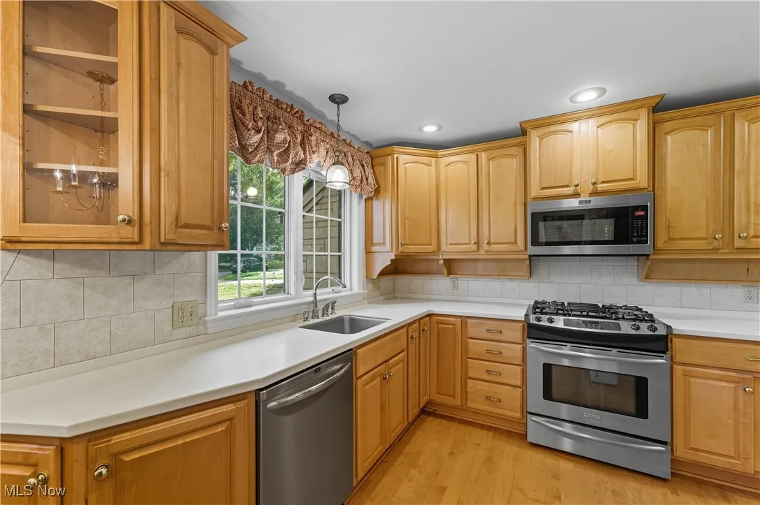 Kitchen with appliances with stainless steel finishes, hanging light fixtures, decorative backsplash, light countertops, and light wood-type flooring