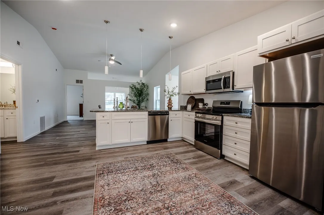 Kitchen with appliances with stainless steel finishes, white cabinetry, vaulted ceiling, a peninsula, and dark wood-type flooring