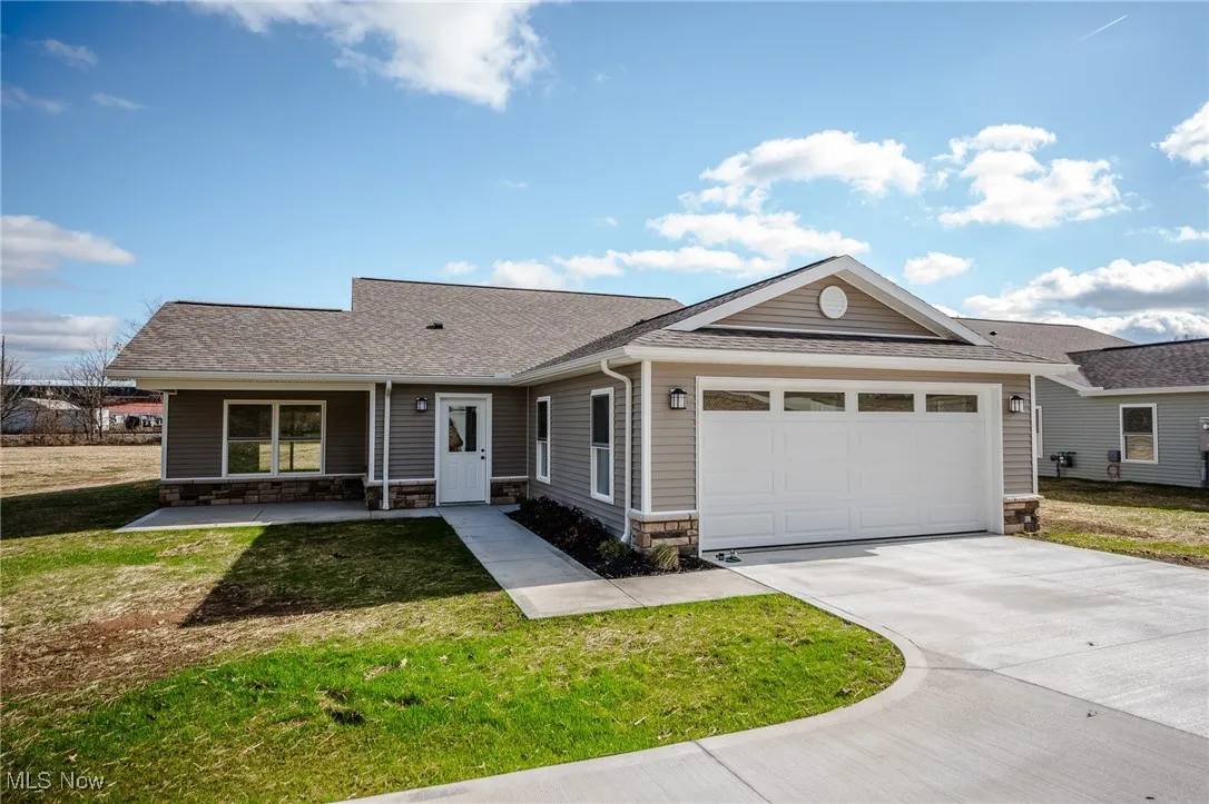 Single story home featuring stone siding, roof with shingles, a front yard, driveway, and a garage